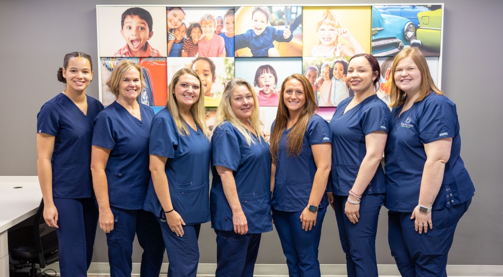 Dental team of smiling professionals in blue scrubs standing together in office setting.